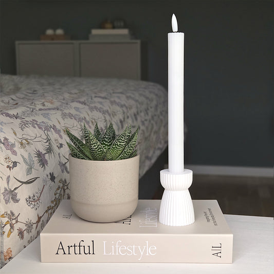 RIBB lysestage i hvid placeret på en bog ved siden af en grøn stueplante – et enkelt udtryk med fokus på bæredygtighed og ro