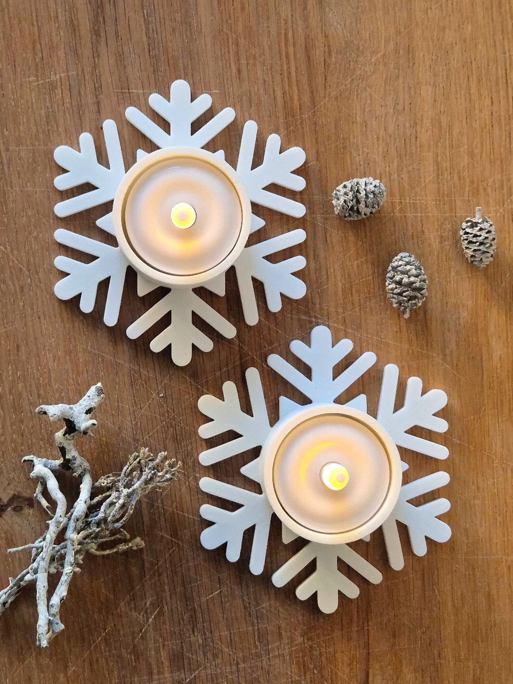 To hvide snefnug fyrfadsstager med LED fyrfadslys på træbord med naturpynt