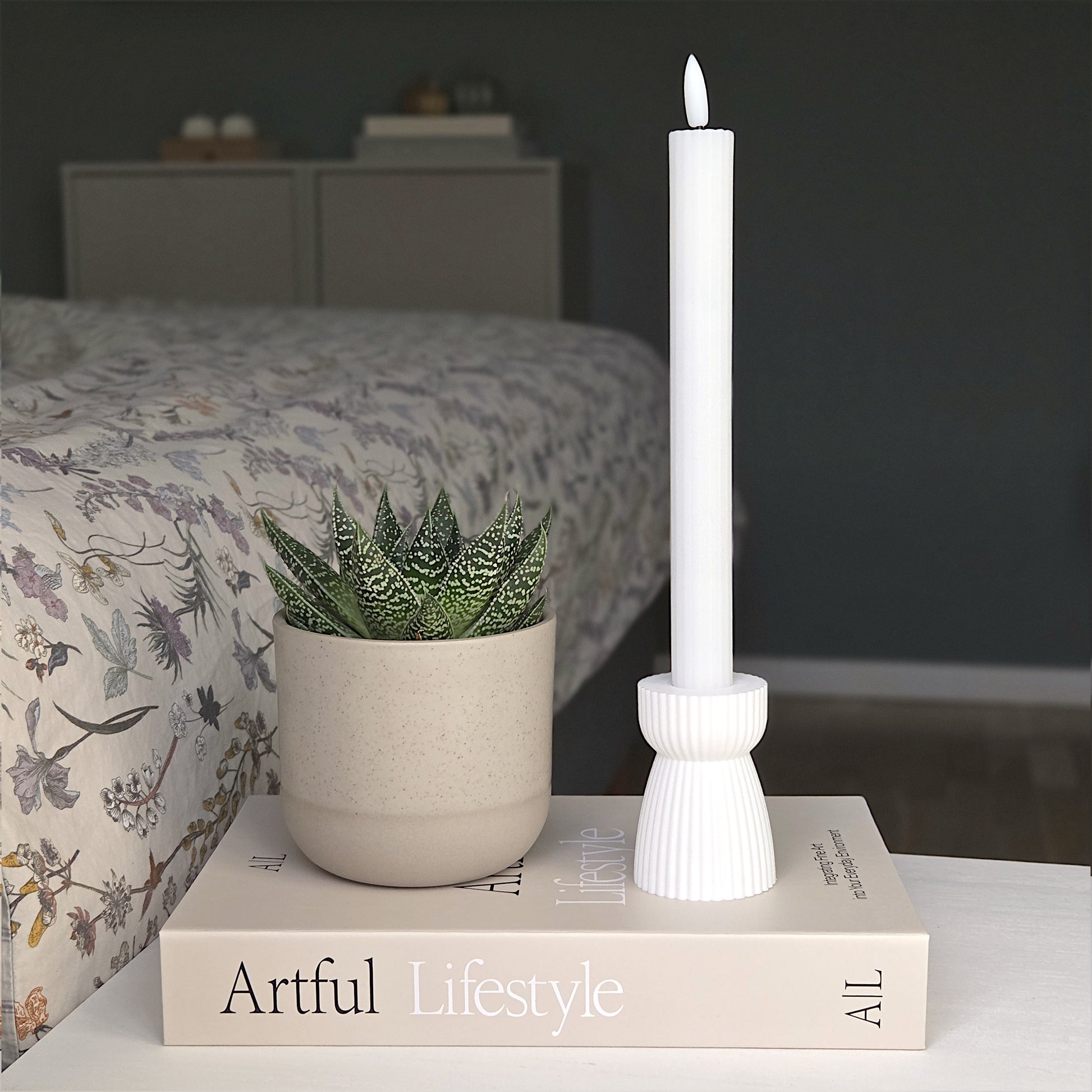 RIBB lysestage i hvid placeret på en bog ved siden af en grøn stueplante – et enkelt udtryk med fokus på bæredygtighed og ro