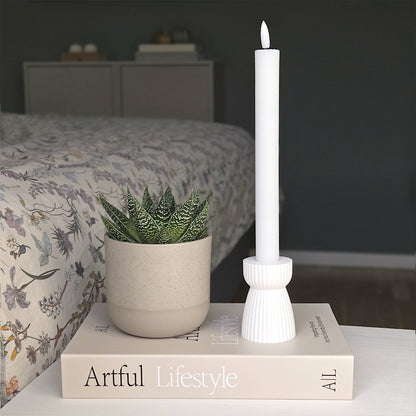 RIBB lysestage i hvid placeret på en bog ved siden af en grøn stueplante – et enkelt udtryk med fokus på bæredygtighed og ro