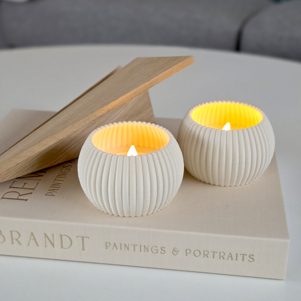 To RIBB fyrfadsstager i cream med ribbet overflade og varm LED-flamme, placeret på en bog og trædetalje – roligt og tidløst dansk design med omtanke og minimal spild.