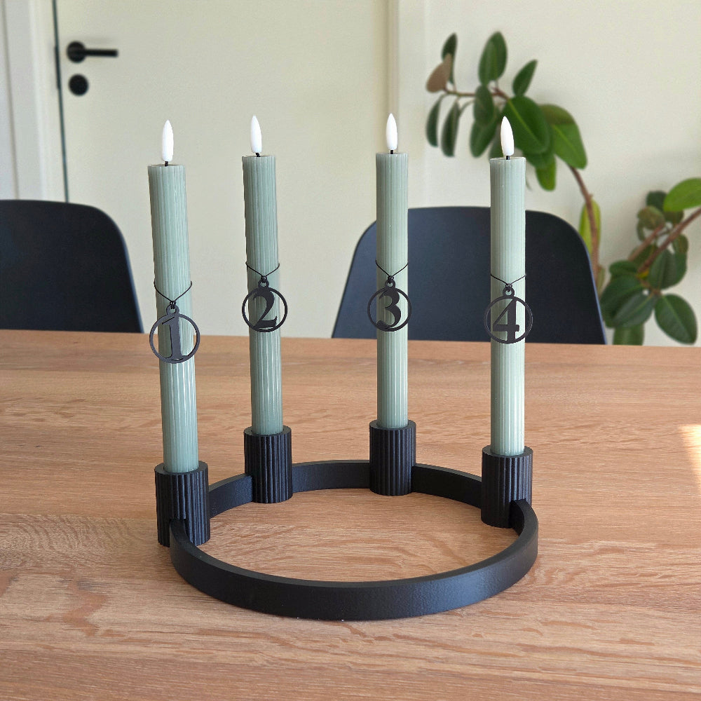 Adventstal 1–4 i sort placeret på grønne kalenderlys i sort adventskrans – rolig julestemning med lys, træ og former valgt med omtanke