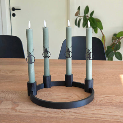 Adventstal 1–4 i sort placeret på grønne kalenderlys i sort adventskrans – rolig julestemning med lys, træ og former valgt med omtanke