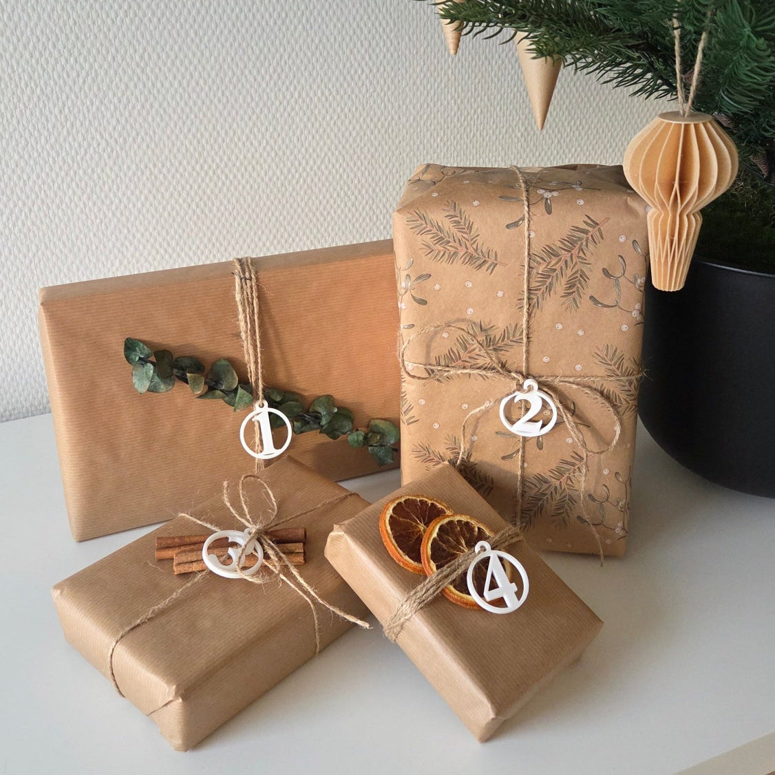 Fire adventstal i hvid placeret på indpakkede gaver – rolig juledekoration med naturmaterialer og små detaljer valgt med omtanke