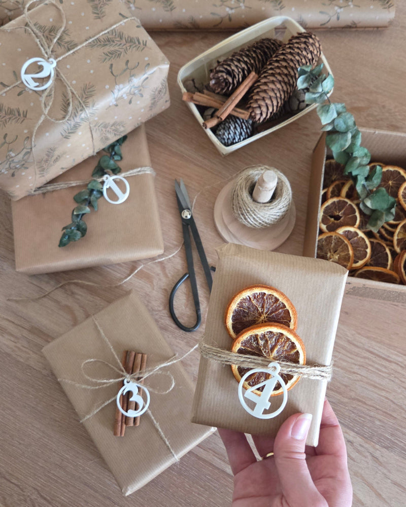 Fire adventstal i hvid placeret på indpakkede gaver – rolig juledekoration med naturmaterialer og små detaljer valgt med omtanke