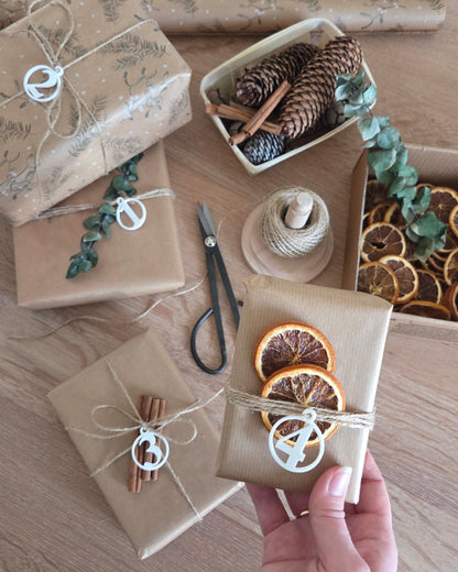 Fire adventstal i hvid placeret på indpakkede gaver – rolig juledekoration med naturmaterialer og små detaljer valgt med omtanke