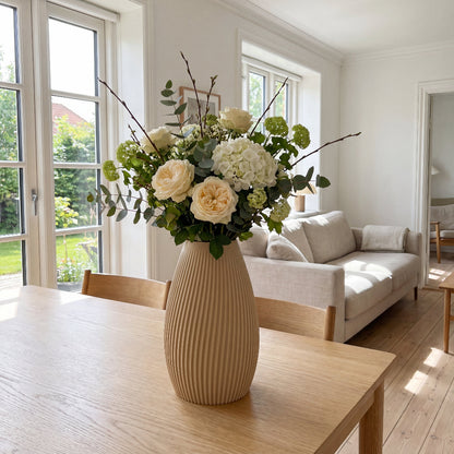 Flute vase i beige fra Hartli med friske blomster på spisebord i et lyst hjem.