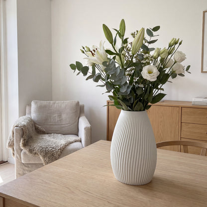 Flute vase i hvid fra Hartli med grønne grene på sidebord i et lyst hjem.