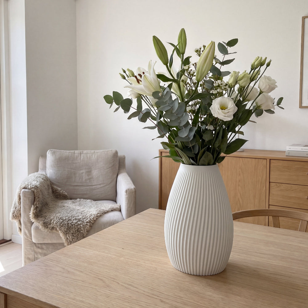 Flute vase i hvid fra Hartli med grønne grene på sidebord i et lyst hjem.