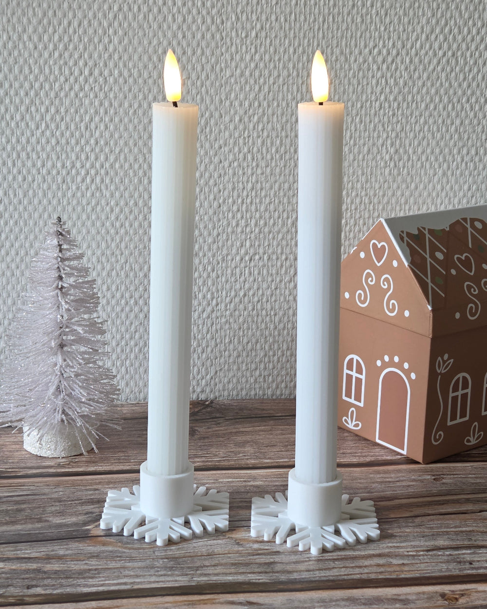 To hvide kronelys i snefnug lysestager på træbord med julepynt i baggrunden