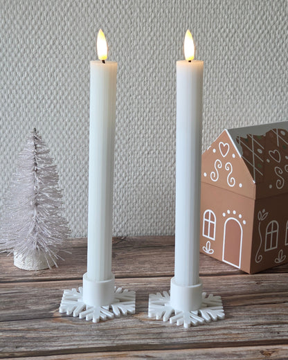 To hvide kronelys i snefnug lysestager på træbord med julepynt i baggrunden